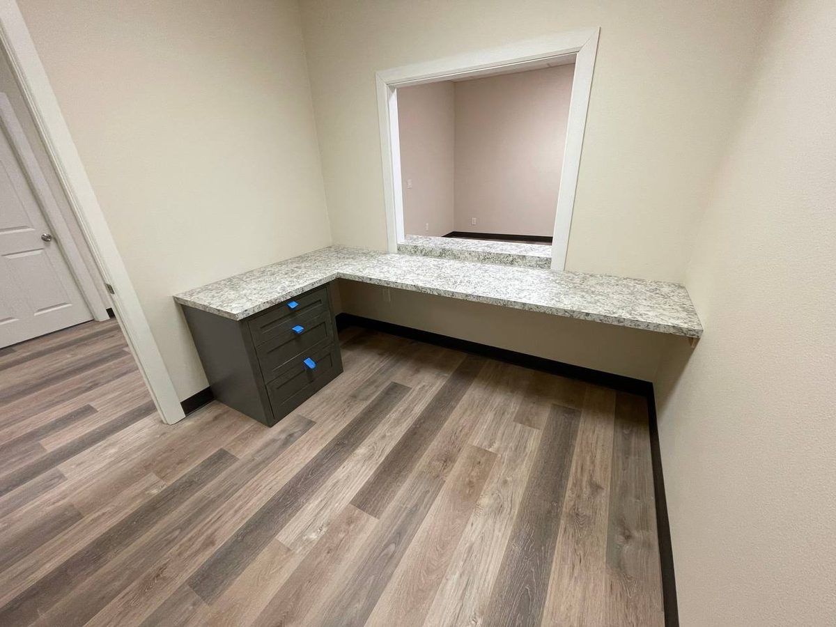 A built-in desk run with a dark countertop and wide-plank flooring in a finished room