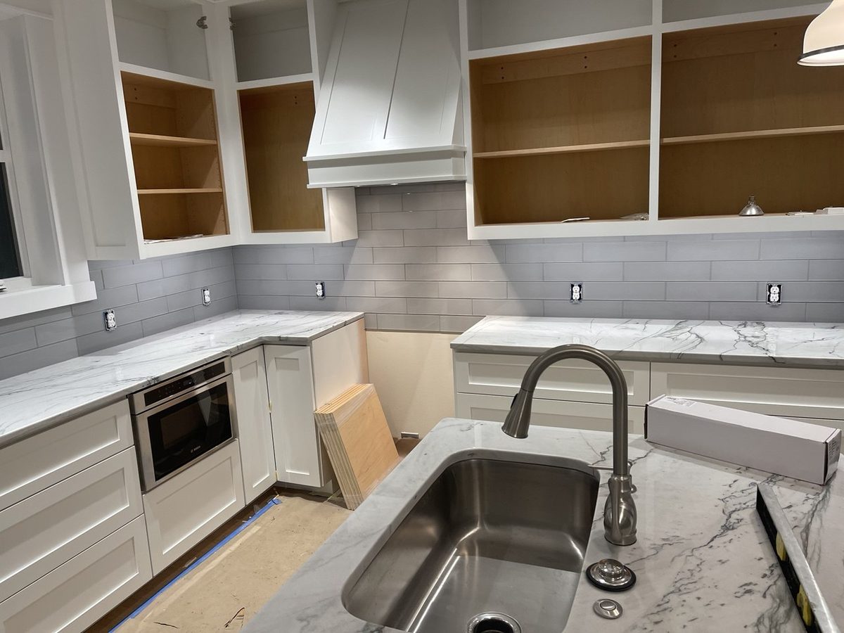 Kitchen installation in progress showing a custom hood surround, quartz counters and an undermount stainless sink