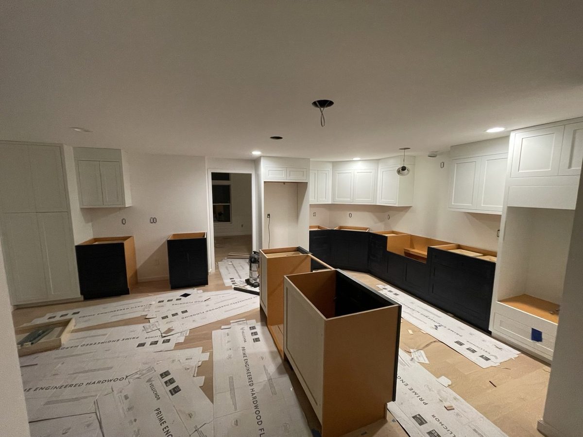 Kitchen installation underway with cabinet boxes being set and the finished floor fully covered in protective paper