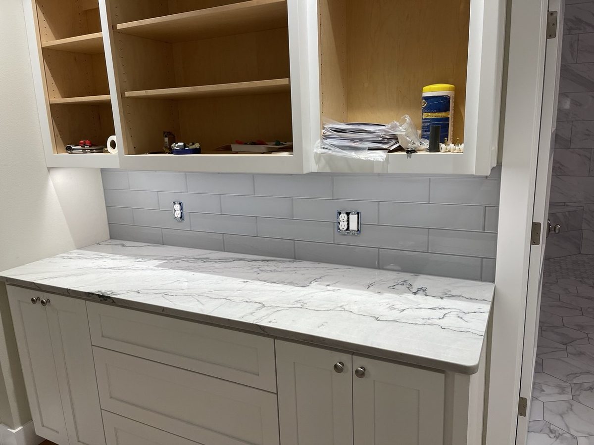 Kitchen installation in progress with white shaker cabinetry, a marble-look countertop and a grey subway backsplash