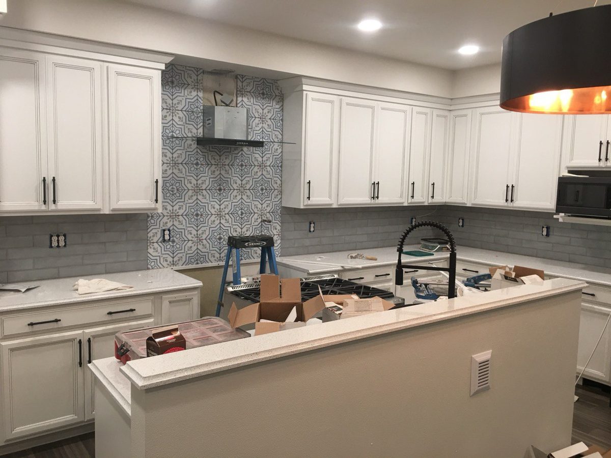 Kitchen remodel in progress with white shaker cabinetry and a patterned tile backsplash behind the range