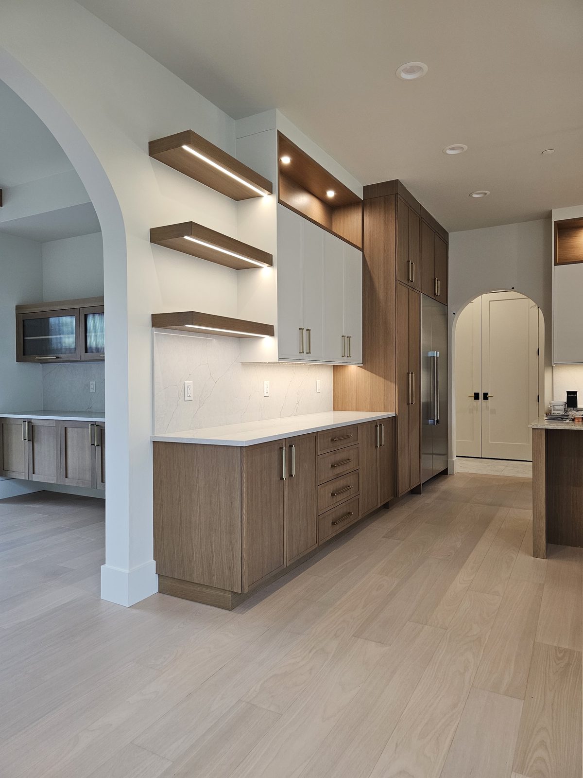 Finished kitchen seen through an arched opening with walnut floating shelves and full-height cabinetry