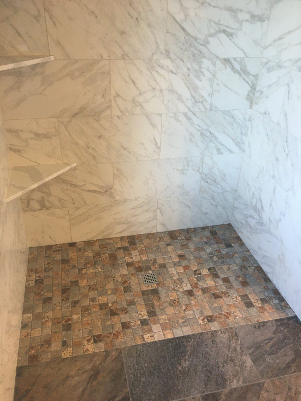 Marble-look shower walls and a tiled floor partway through installation