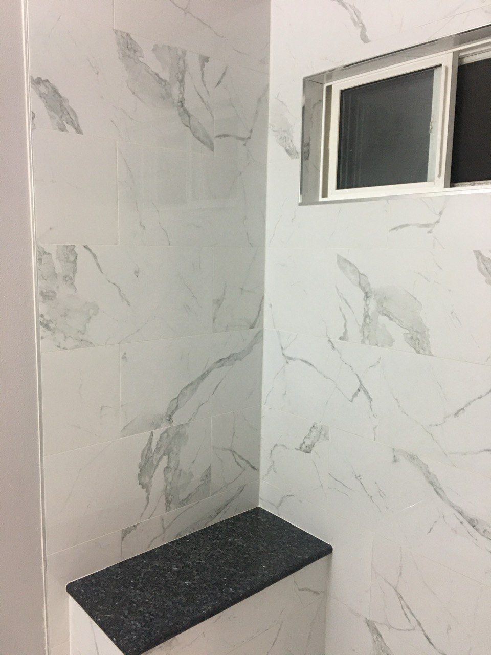 Finished marble-look tiled shower with a window and a stone sill