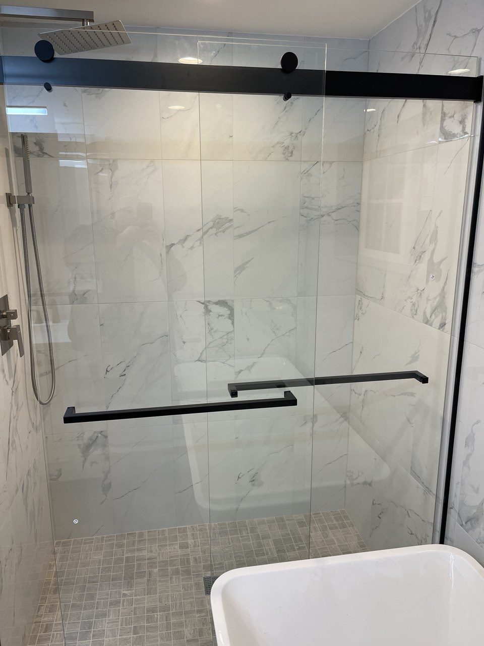Finished shower with a black-framed sliding glass door and marble-look tiled walls