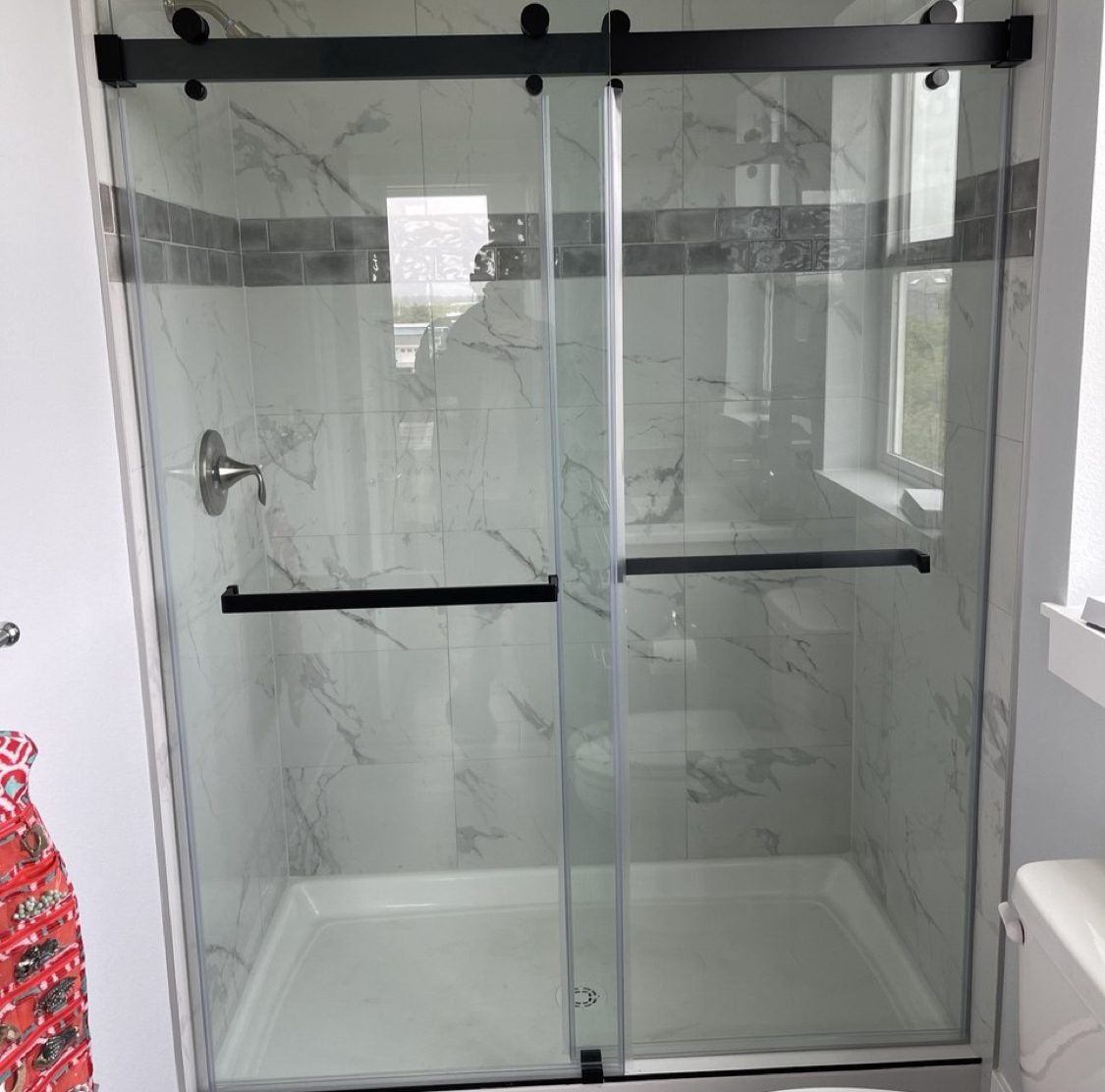 Finished tub-shower alcove tiled in marble-look porcelain with a mosaic accent band and a black-framed sliding glass door