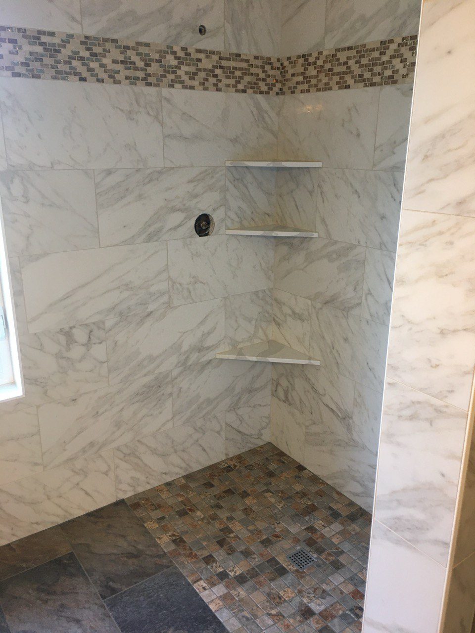 Shower walls tiled in marble-look porcelain with a pebble-tiled niche, during construction