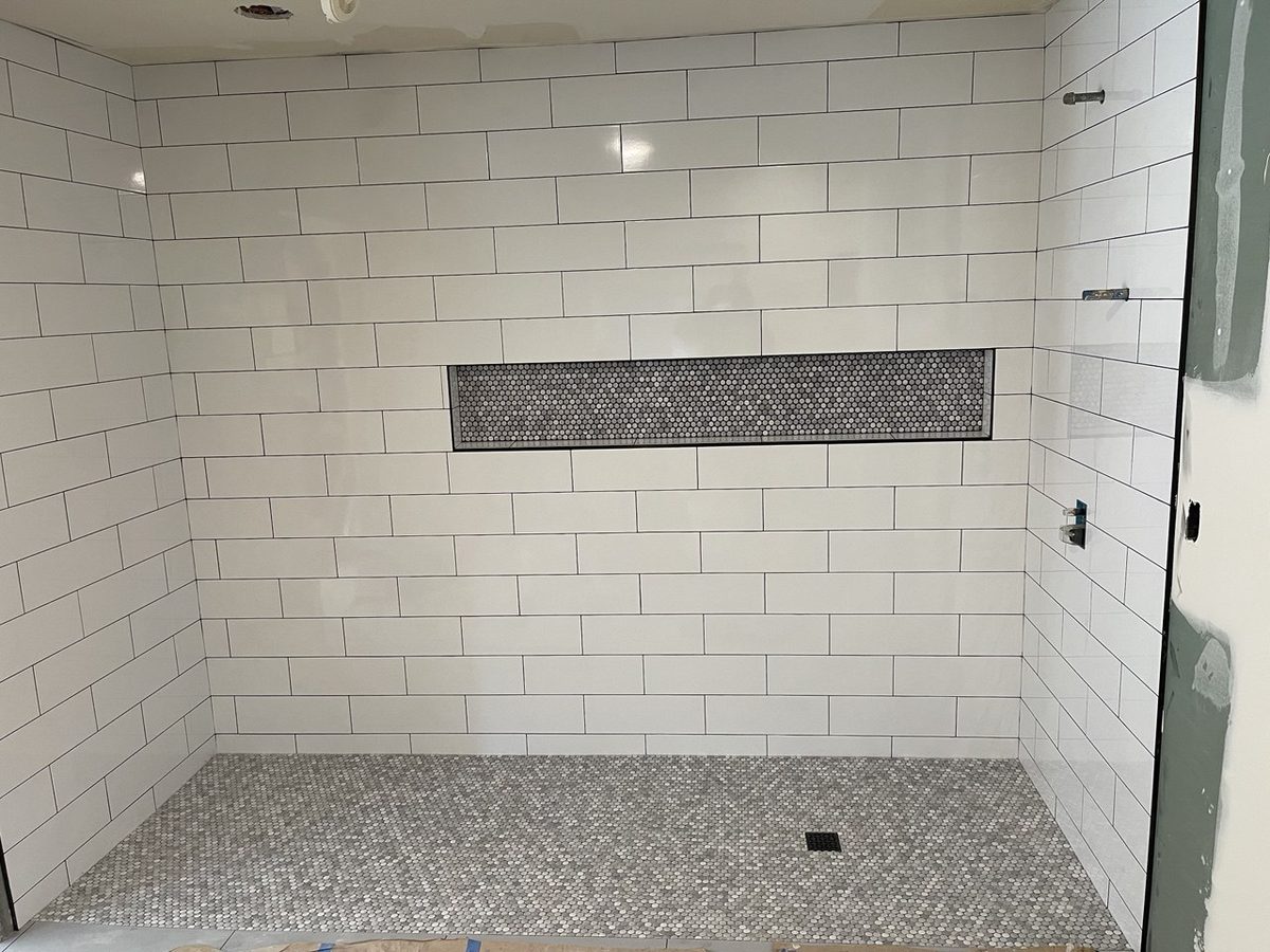 Finished shower in white subway tile with a long recessed niche and a pebble tile floor
