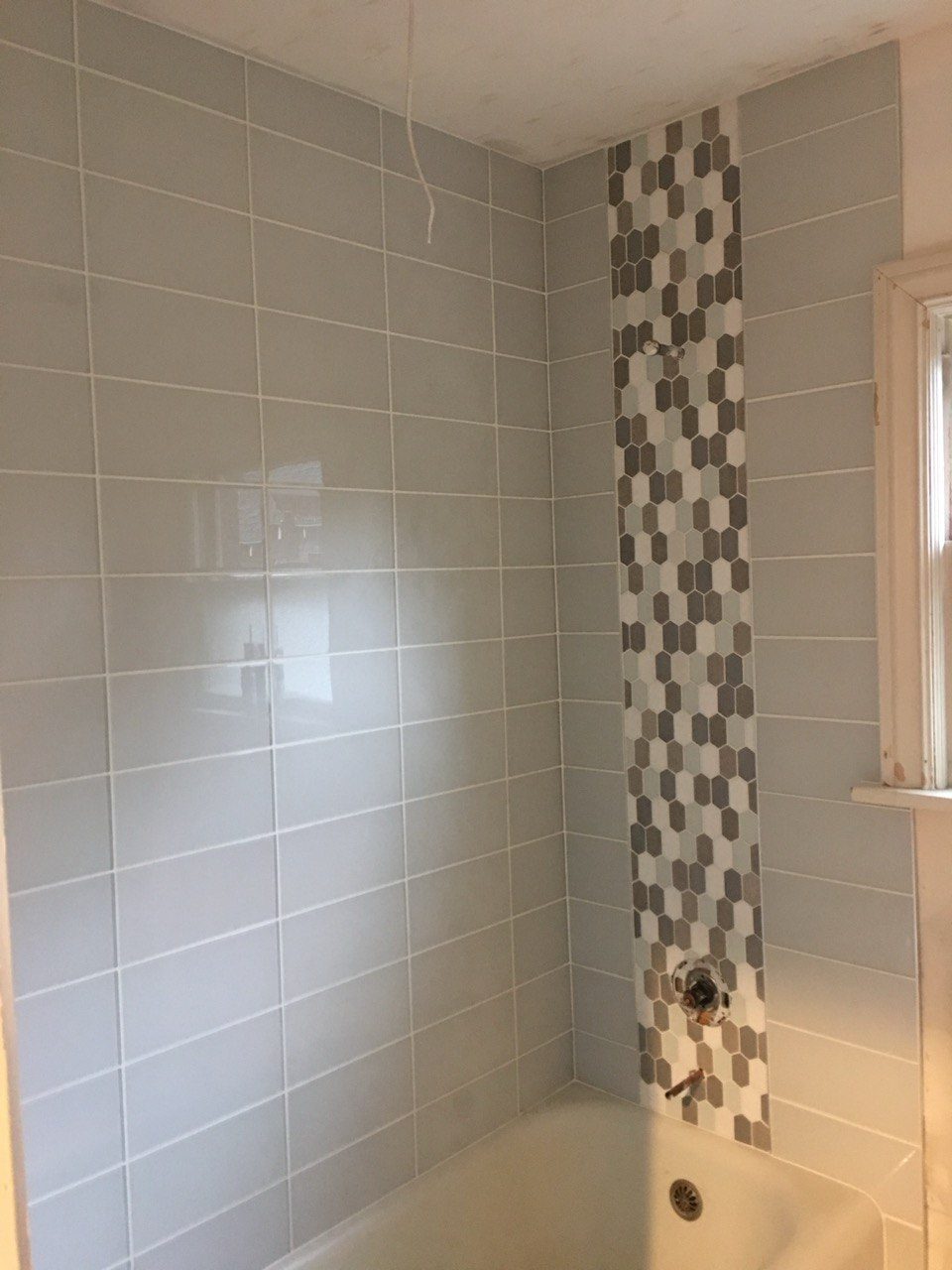 Finished tub surround in subway tile with a vertical mosaic accent strip