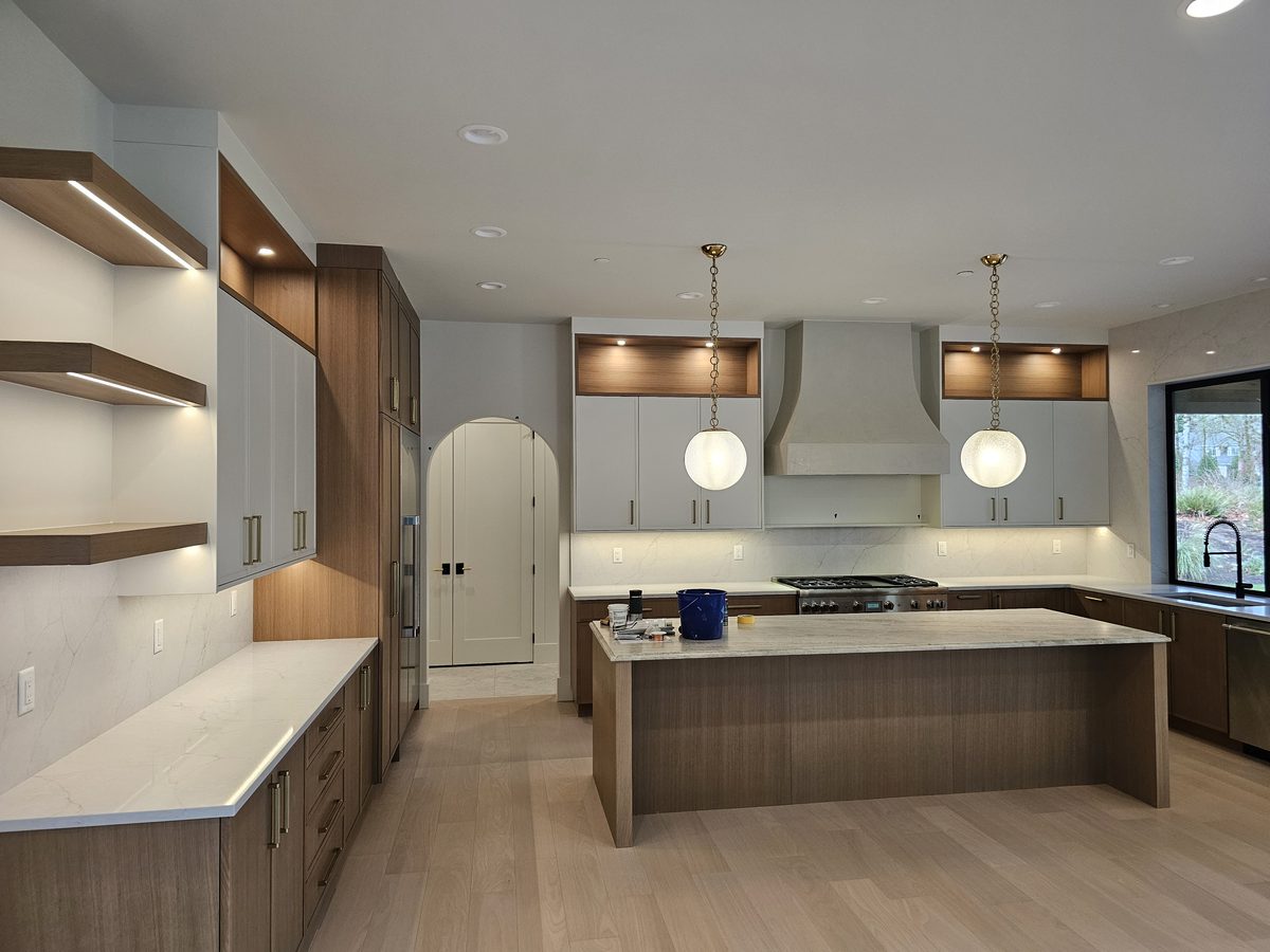 Finished open-plan kitchen with white perimeter cabinetry, a walnut island, custom hood surround and globe pendants