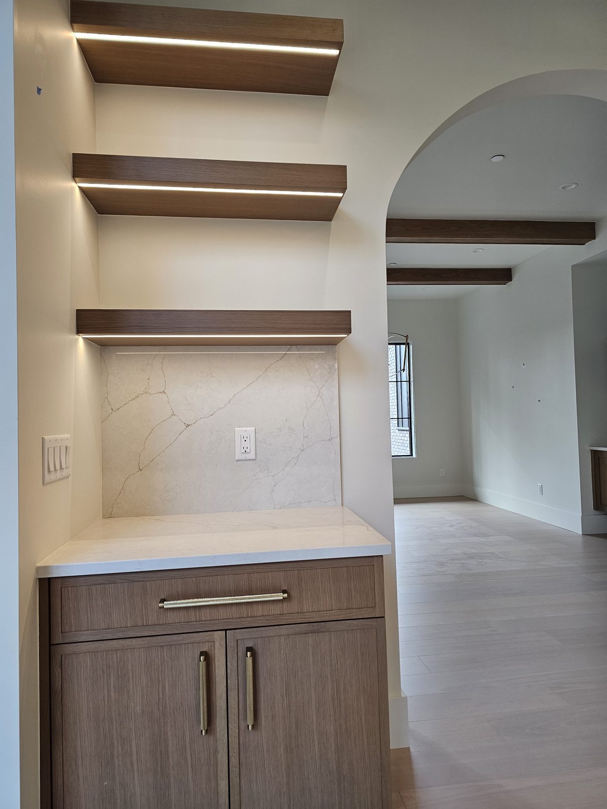 Walnut floating shelves beside an arched entry in a finished kitchen